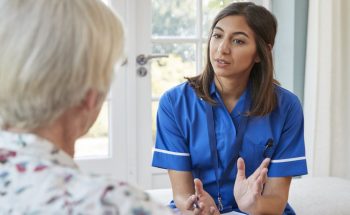 Senior woman talking to young care nurse on home visit