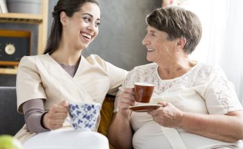 Smiling volunteer drinking coffee with a senior patient in a nursing home